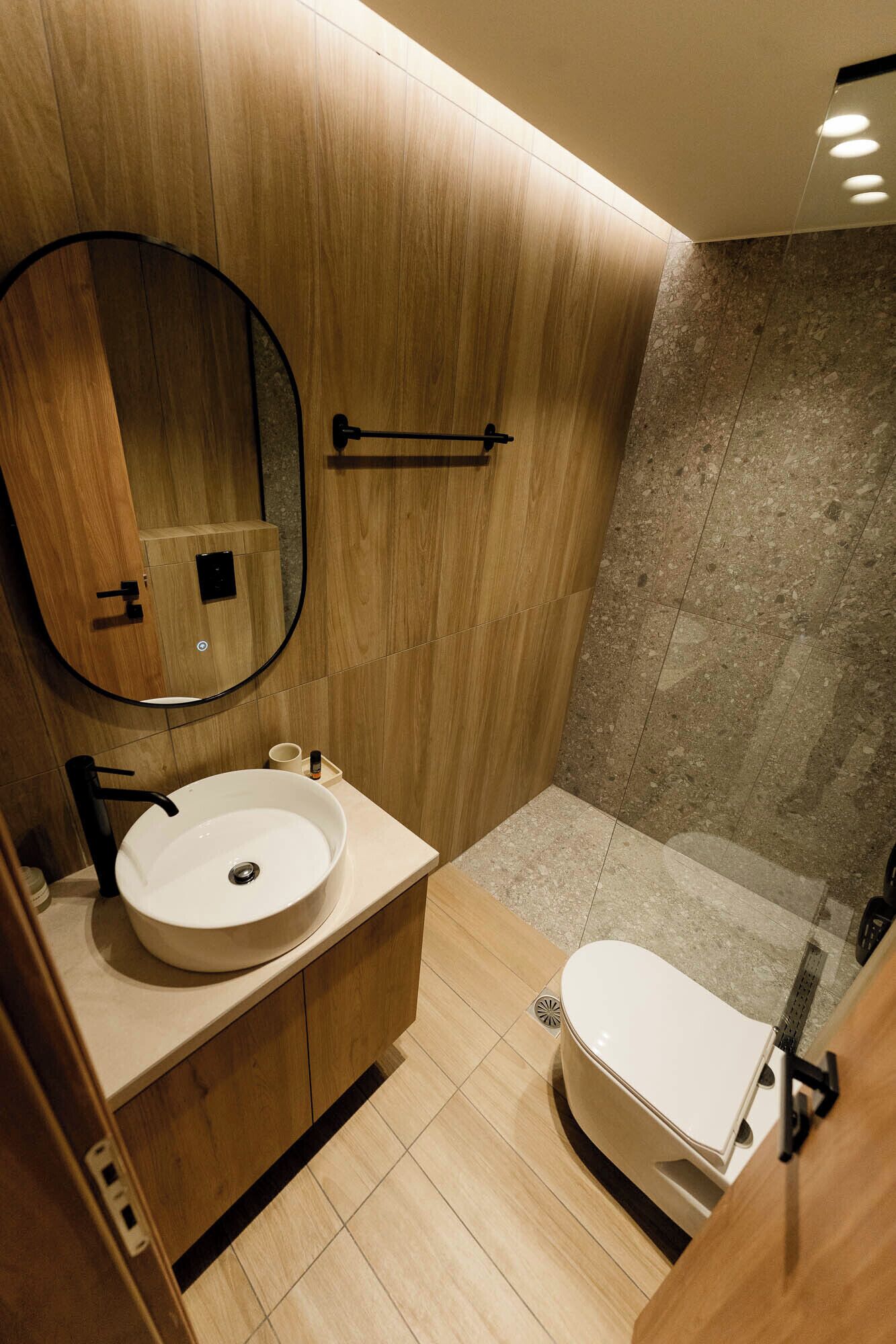 A modern bathroom with a wooden vanity, a round sink, a toilet, and a shower area.