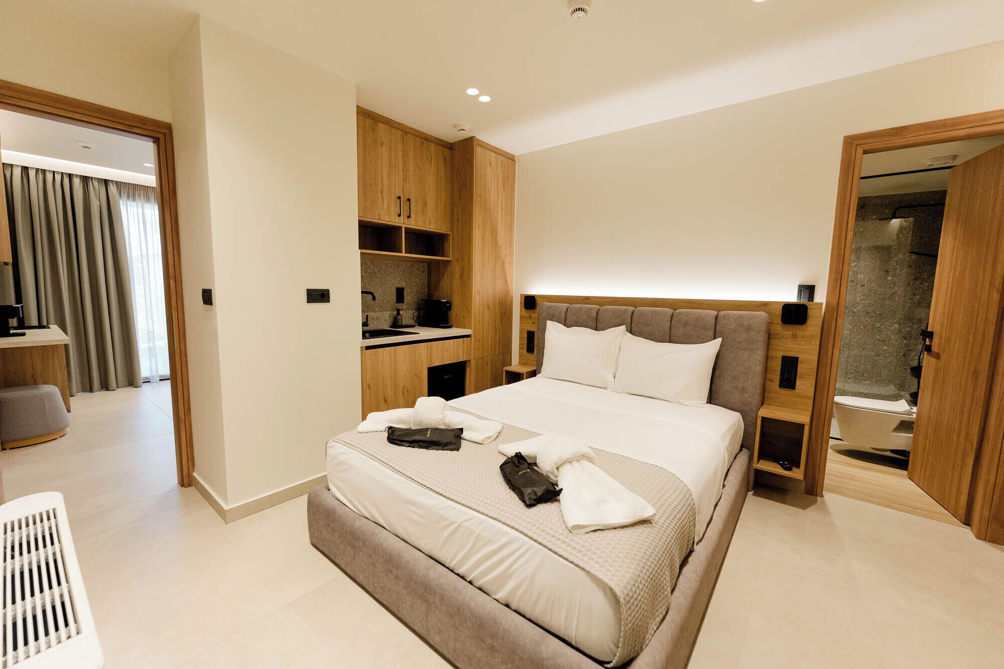 Una habitación de hotel moderna con una cama grande, armario empotrado, kitchenette y baño con cabina de ducha de vidrio.