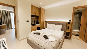 Una habitación de hotel moderna con una cama grande, armario empotrado, kitchenette y baño con cabina de ducha de vidrio.