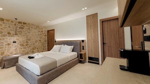 Un dormitorio moderno con pared de piedra, cama con cabecera de madera, mesita de noche, armario empotrado y baño con lavabo y espejo negros.