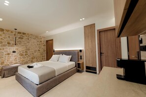 A modern bedroom with a stone wall, a bed with a wooden headboard, a nightstand, a built-in wardrobe, and a bathroom with a black sink and mirror.