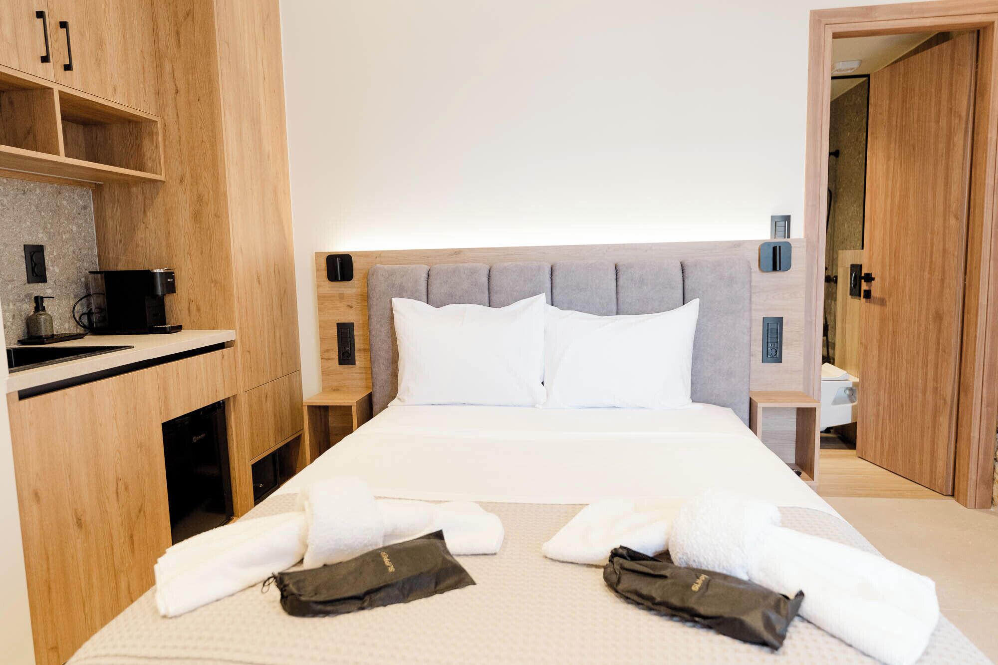 Une chambre d’hôtel avec un lit, une armoire en bois, une table de chevet avec une machine à café et une porte de salle de bain.