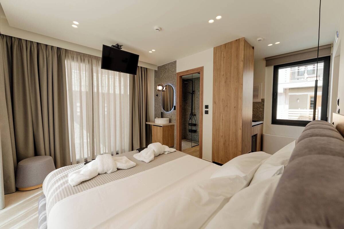 A modern hotel room with a large bed, a TV, a bathroom with a mirror, and a window.