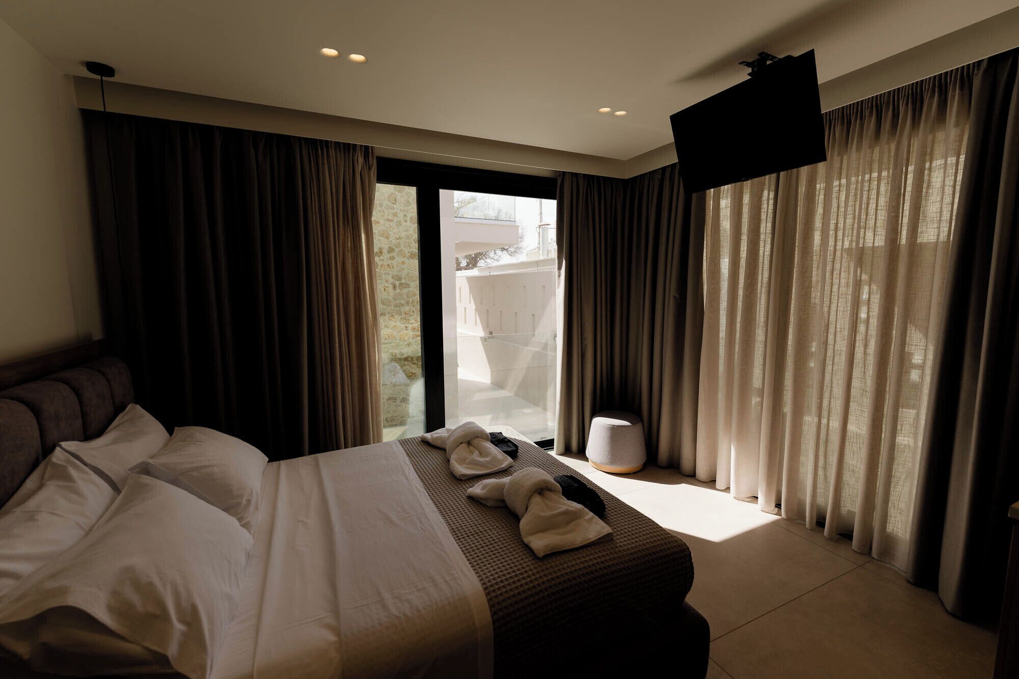 A hotel room with a bed, a TV, and a view of the outside.