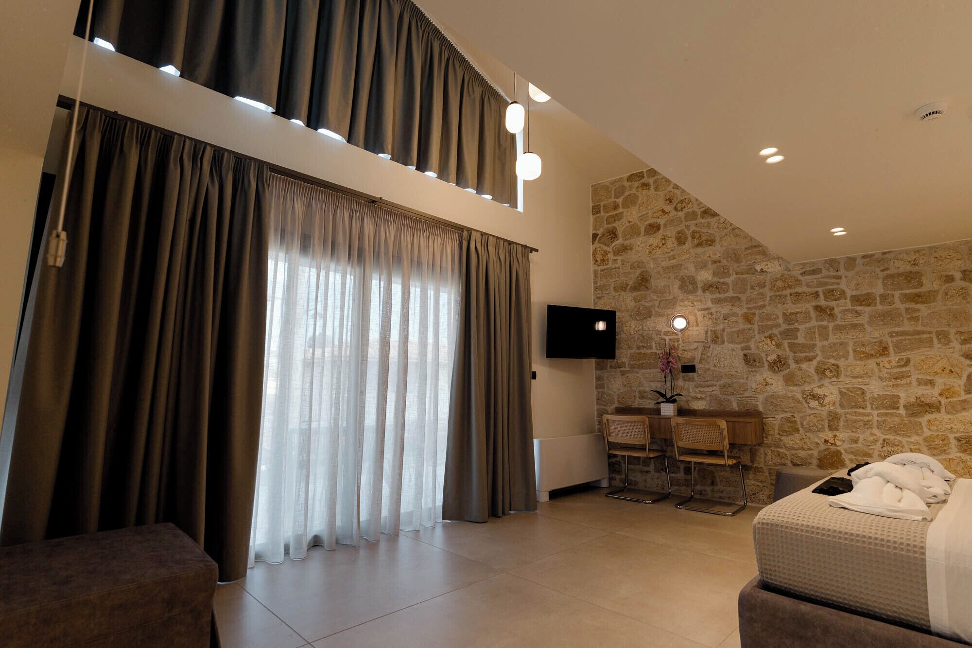 Una habitación moderna con pared de piedra, un televisor de pantalla plana, un sofá, una mesa de comedor con sillas y una cama con cubrecama blanco.