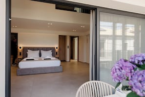 A modern hotel room with a large bed, a small table, and a view through a glass door.