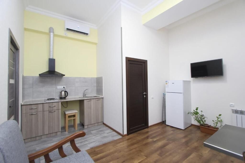 A compact kitchen with a stove, sink, and a TV mounted on the wall.