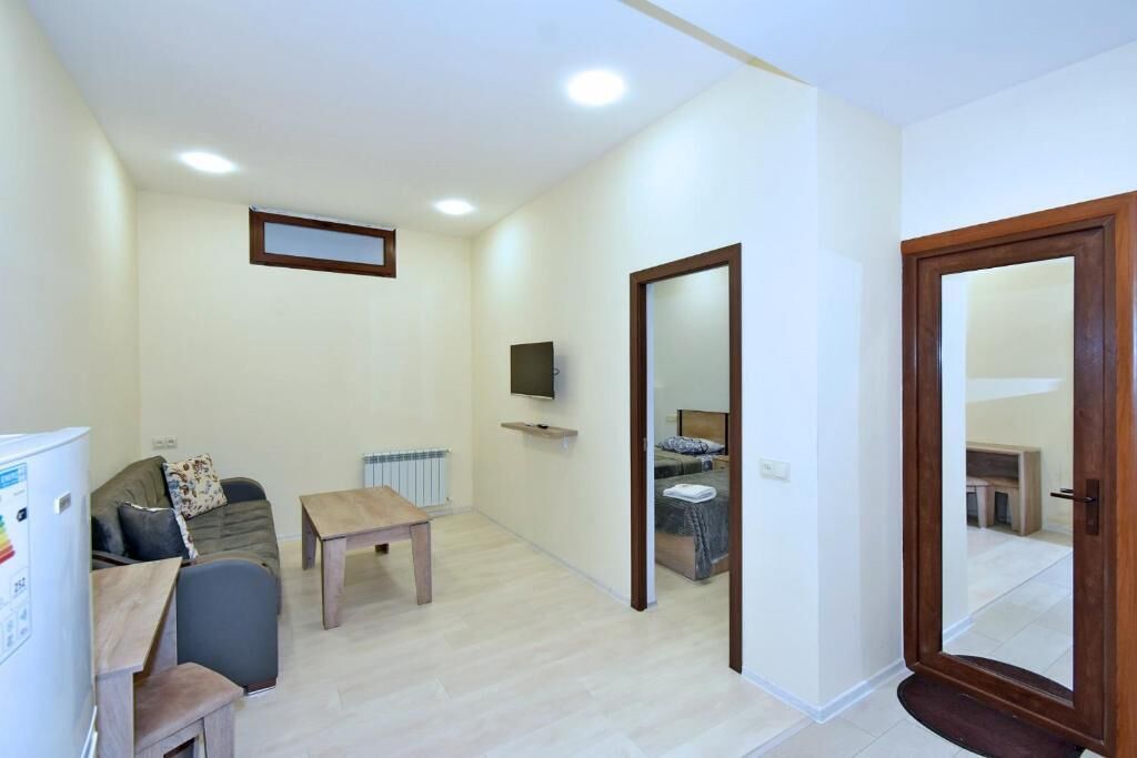 Un espacio habitable compacto con sofá, una mesita, televisor montado en la pared y una puerta de madera.