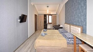 Ett hotellrum med en säng, ett bord, en tv och utsikt över korridoren.