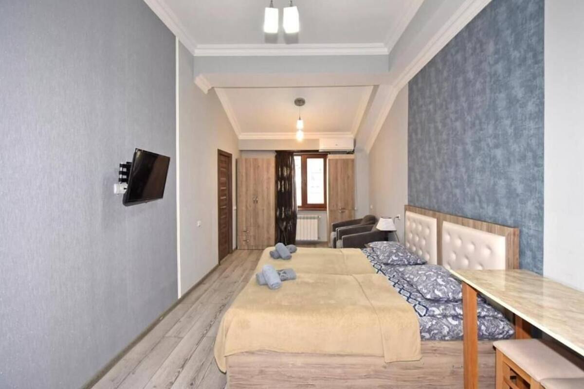 A hotel room with a bed, a table, a TV, and a view of the hallway.