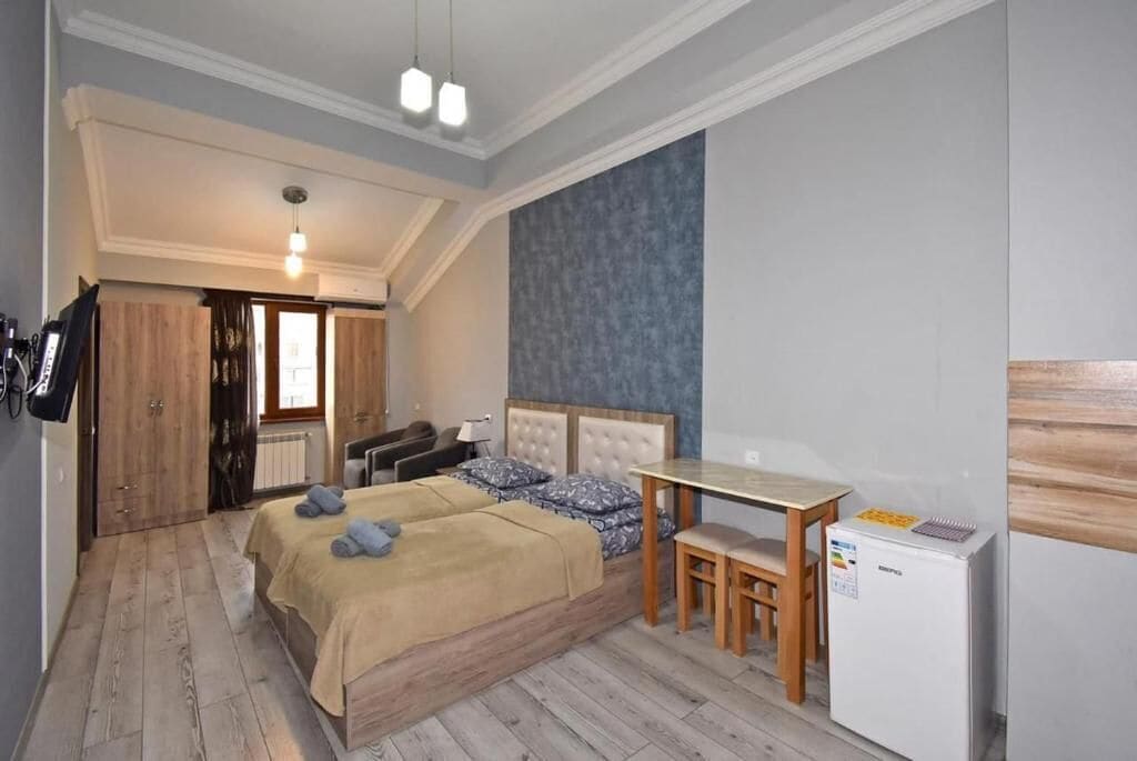 A bedroom with a bed, a desk, a chair, a refrigerator, and a wardrobe.