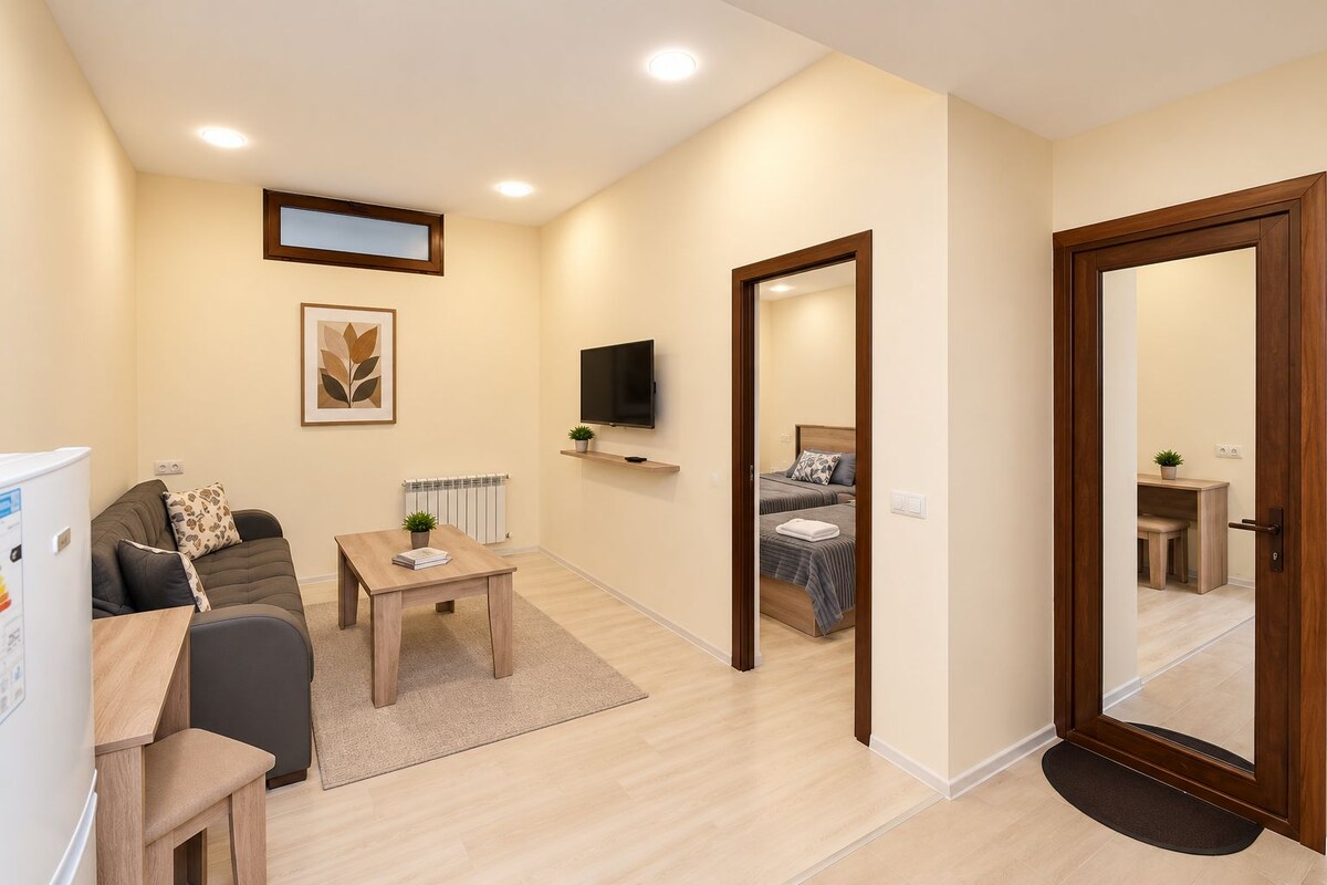 Una sala moderna con un sofá, una mesita de centro, un televisor y una cama al fondo.