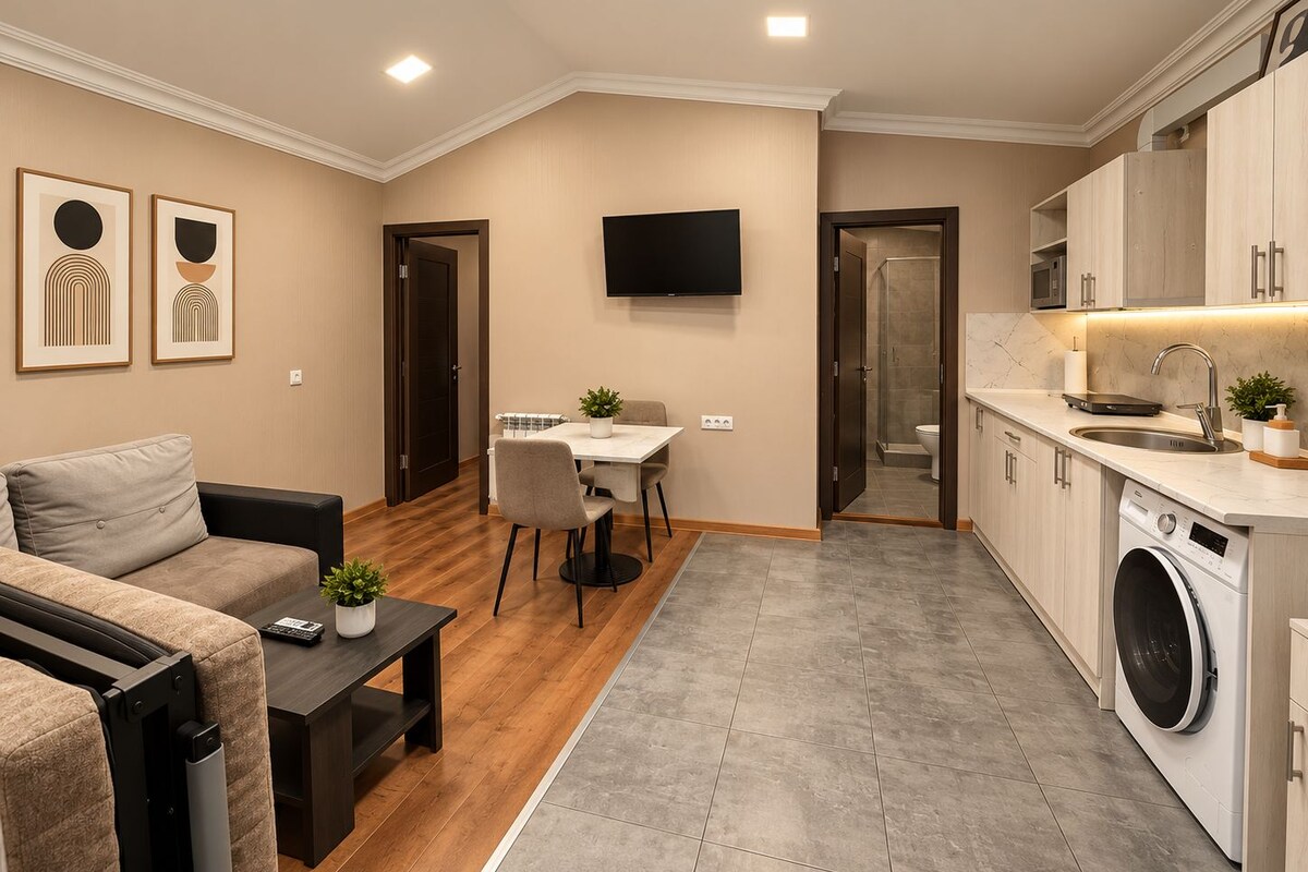 Un espacio habitable compacto con sofá, mesa de comedor, televisor, cocina con lavadora y zona de ducha.