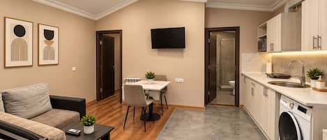 Un espacio habitable compacto con sofá, mesa de comedor, televisor, cocina con lavadora y zona de ducha.