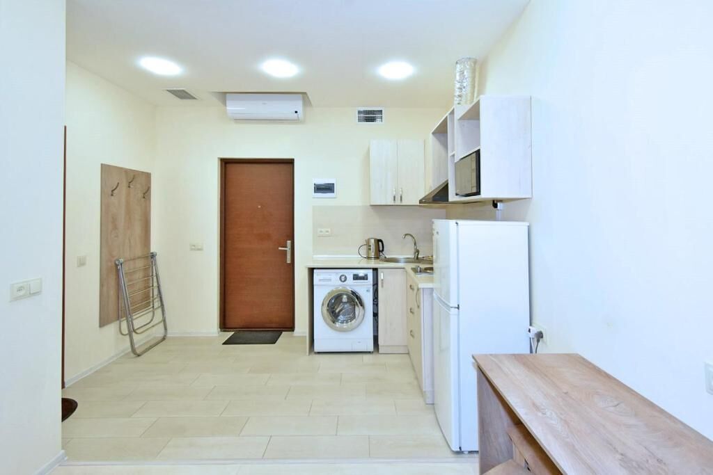Uma cozinha compacta com máquina de lavar, micro-ondas e um banco de madeira.