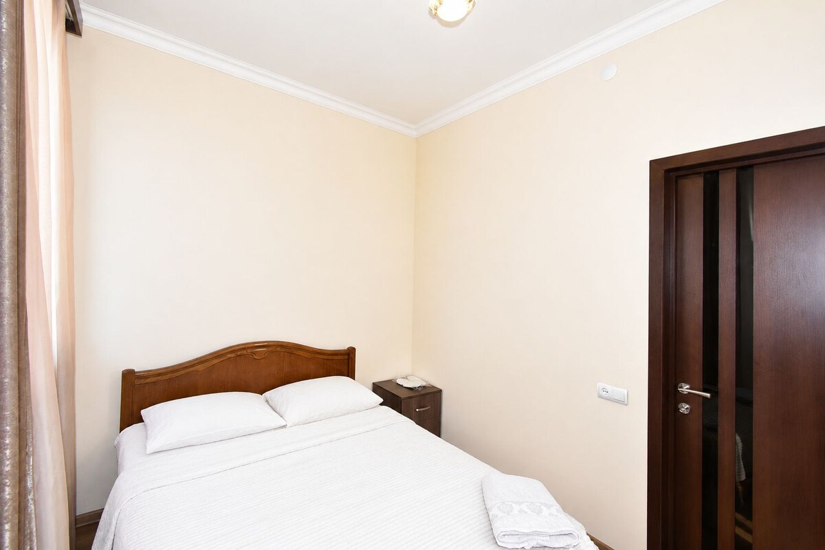 Una habitación de hotel con una cama de madera, una mesita de noche, una puerta y una lámpara.
