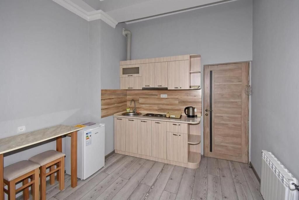Una cucina compatta con forno a incasso, lavello e frigorifero. Si nota una panca in legno e una porta sulla destra.