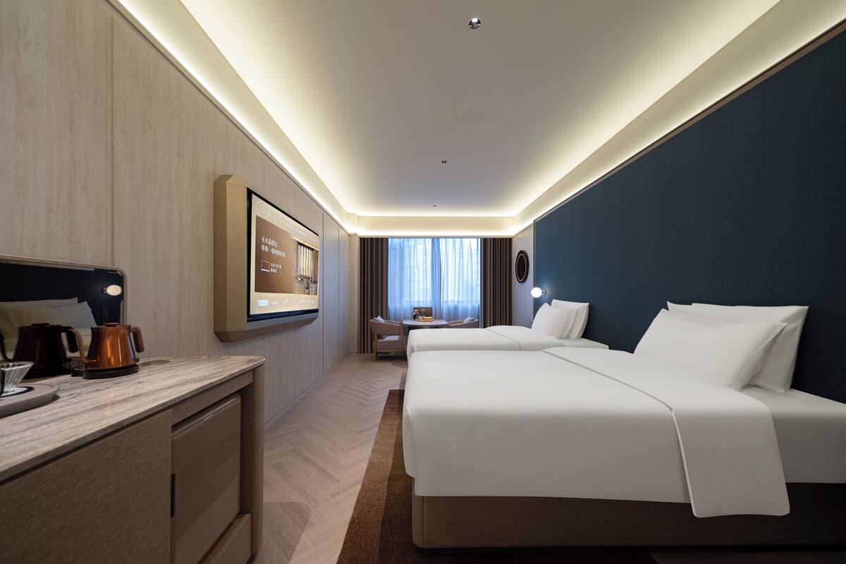A hotel room with a bed, bedside table, and a desk with a lamp.