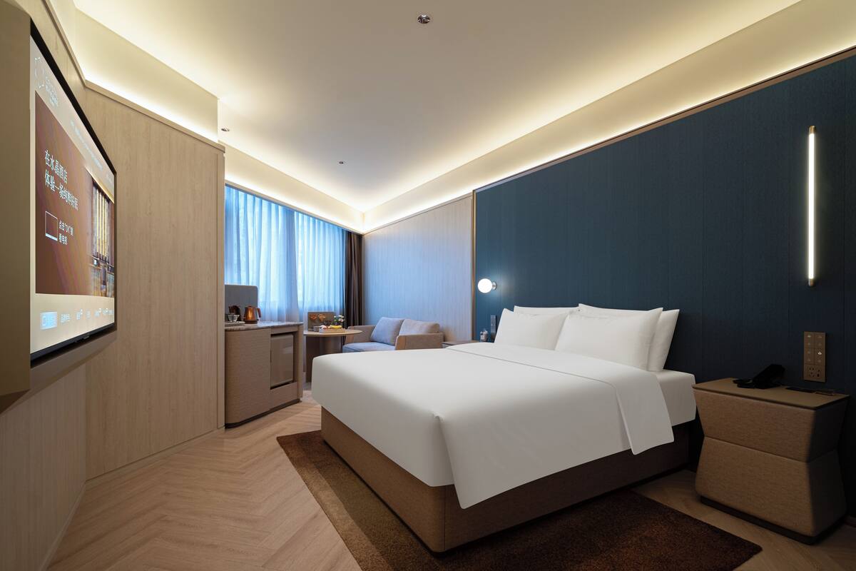 A modern hotel room with a large bed, bedside tables, a desk, and a TV screen.