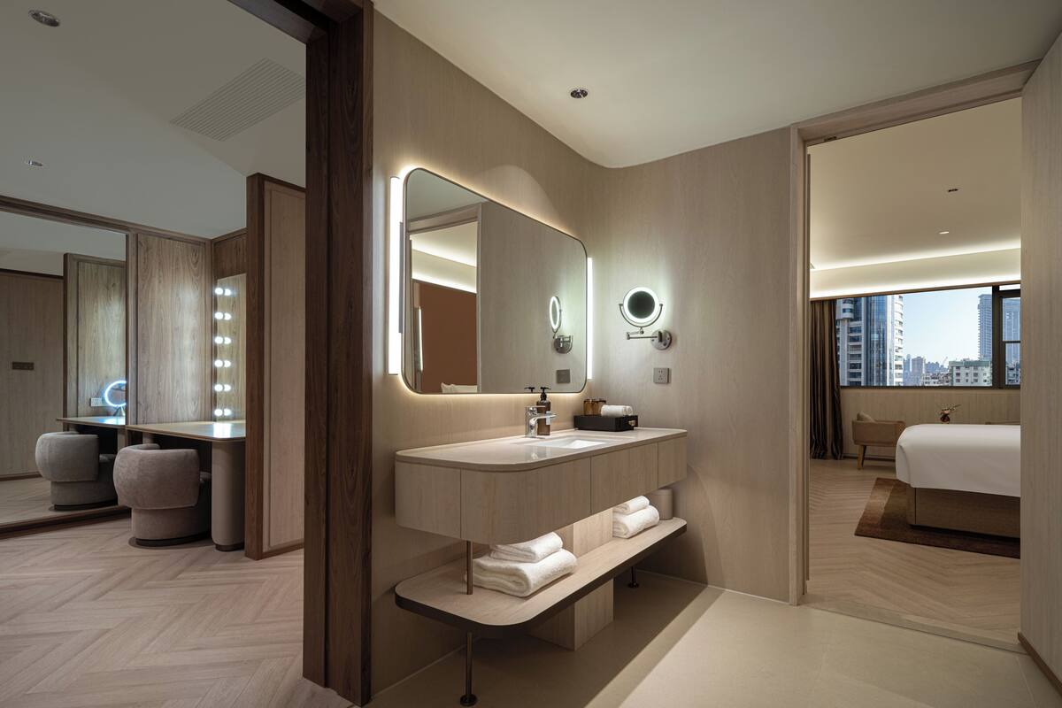 A modern hotel bathroom with a vanity, mirror, and built-in bench.