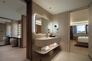 A modern hotel bathroom with a vanity, mirror, and built-in bench.