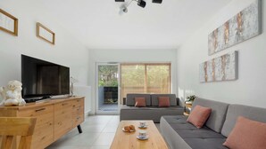 A modern living room with a flat-screen TV, wooden coffee table, grey sofa, and artwork on the walls. - Comfortable Studio with a Terrace | Near the Beach (Międzywodzie)