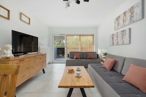 A modern living room with a flat-screen TV, wooden coffee table, grey sofa, and artwork on the walls. - Comfortable Studio with a Terrace | Near the Beach (Międzywodzie)