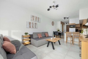 Een moderne woonkamer met een grijze bank, een houten salontafel en een keukenhoek met houten kasten en een eettafel.