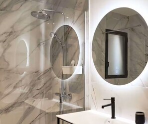 A modern bathroom with a glass-enclosed shower, a round mirror, and a white sink. - Magnificent sea View From This Apartment (Agde)
