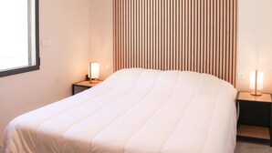 Quarto de hotel com uma cama, duas mesas de cabeceira, uma janela e um painel de ripas de madeira.
