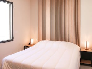A hotel room with a bed, two bedside tables, a window, and a wooden slat wall. - Magnificent sea View From This Apartment (Agde)
