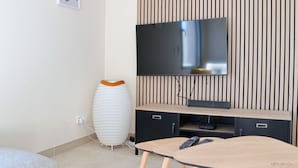 Sala de estar moderna com televisão de tela plana fixada em parede de madeira, um vaso decorativo branco e uma pequena mesa com controle remoto.