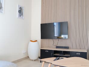 A modern living room with a flat-screen TV mounted on a wooden wall, a white decorative vase, and a small table with a remote control. - Magnificent sea View From This Apartment (Agde)