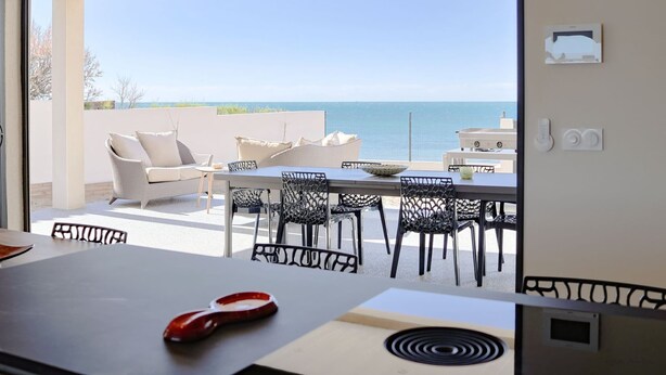 Uma área de refeições com vista para o mar, mesas ao ar livre e uma cozinha moderna.
