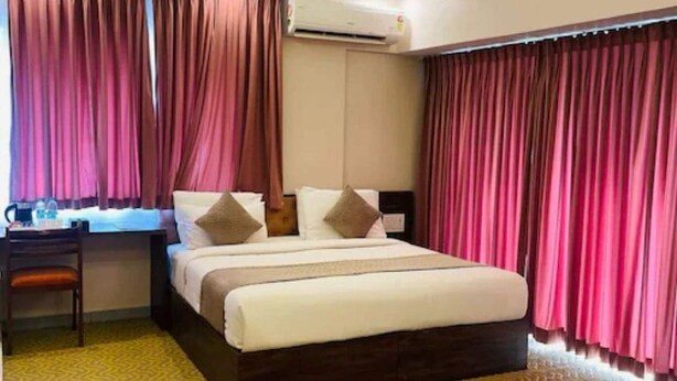 Quarto de hotel com uma cama, uma escrivaninha com cadeira, ar condicionado e cortinas.