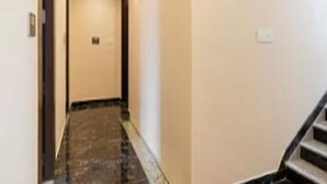 Um corredor estreito com chão de mármore, uma porta no final e uma escadaria à direita.