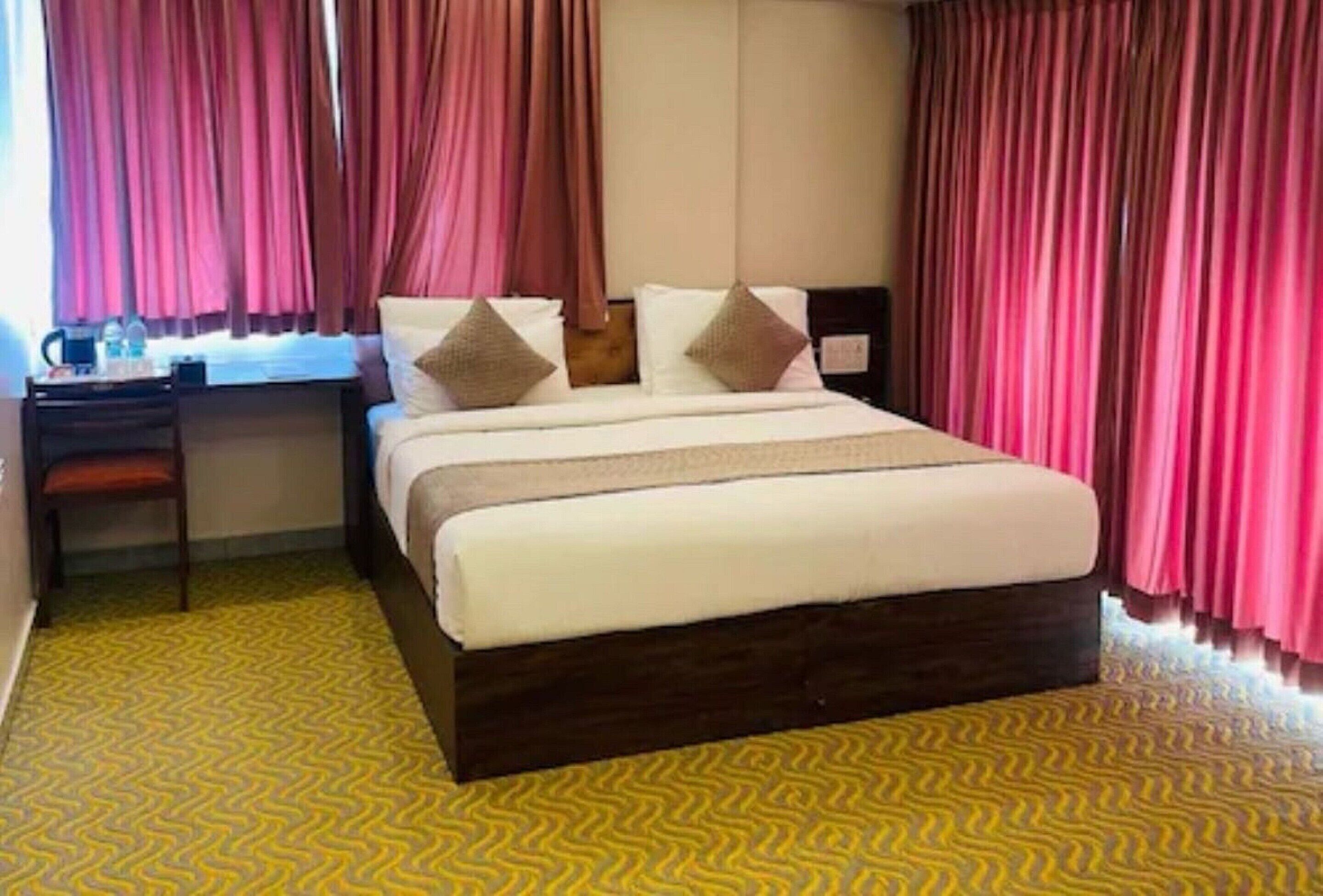 A hotel room with a bed, a desk, and curtains.