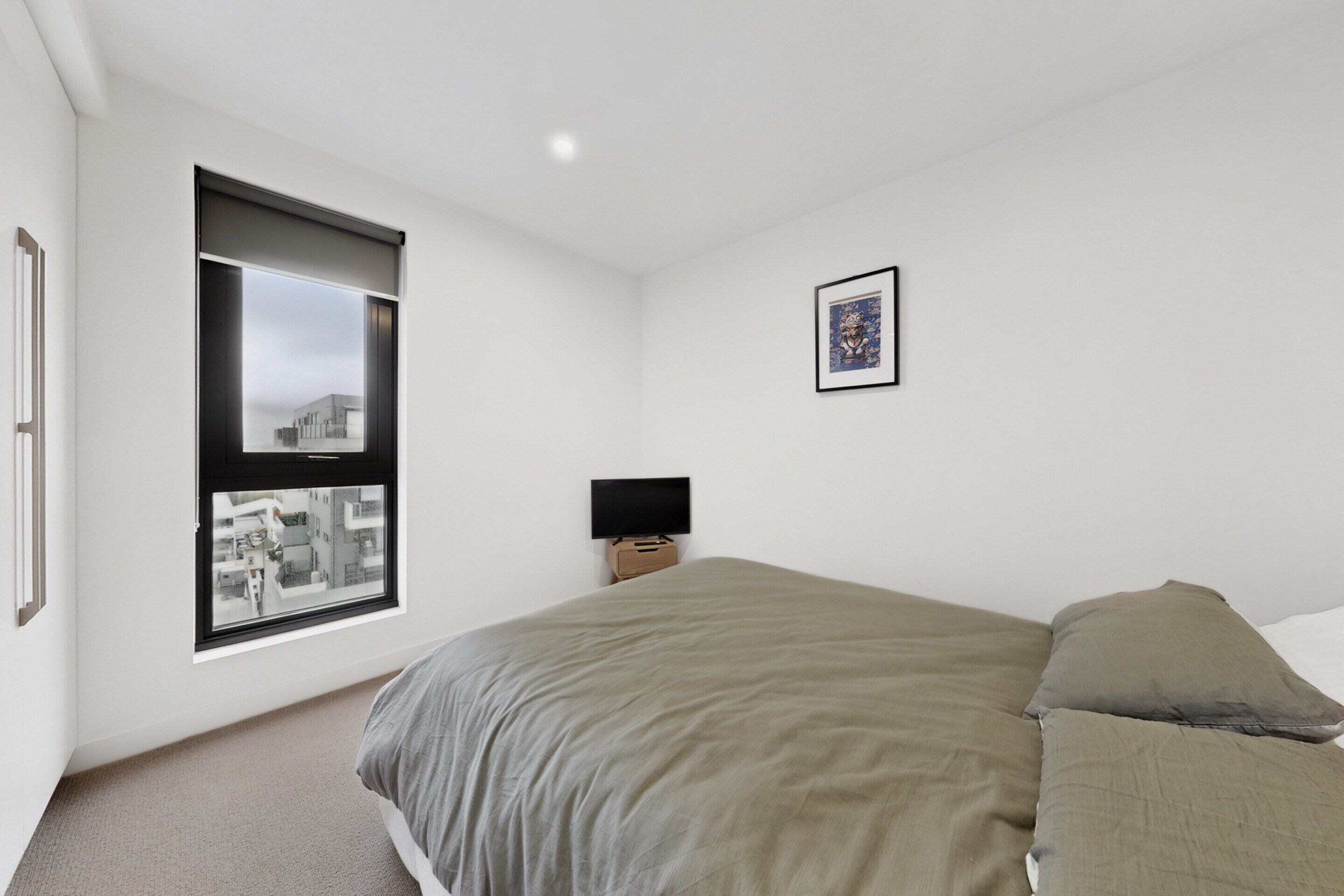 A bedroom with a bed, a window, a wall-mounted TV, and a framed picture.