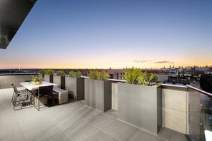 A rooftop terrace with a table and chairs, potted plants, and a cityscape view at sunset. - Modern Living in the Heart of Hawthorn East (Melbourne)