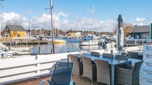 Ein Yachthafen mit vertäuten Booten, ein Holzdeck mit Außenbestuhlung und Gebäude im Hintergrund.