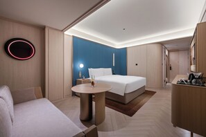 A modern hotel room with a bed, bedside table, round table, and a desk with a chair. - Crystal Hotel Wusi Square Wheat Island (Qingdao)