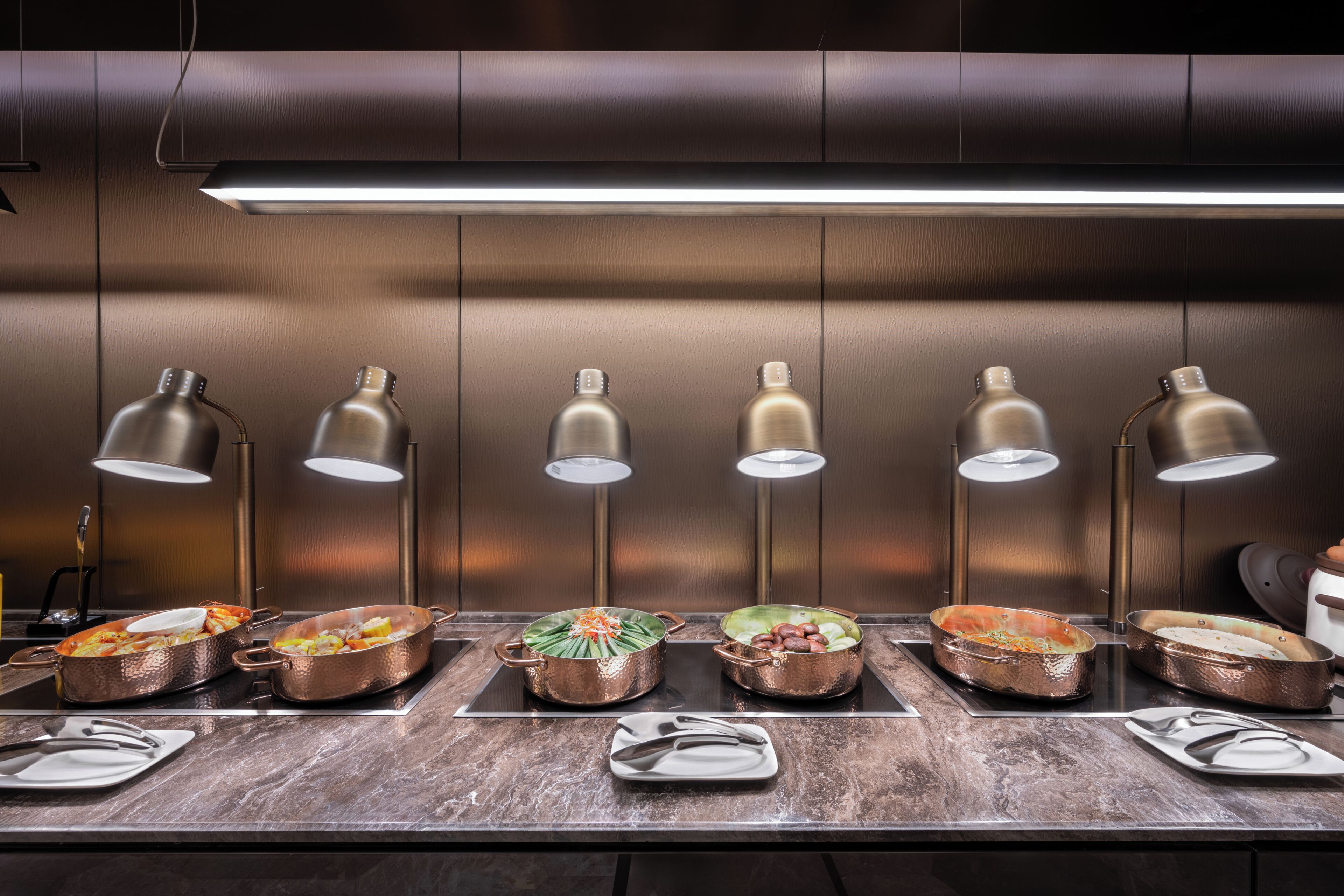 A kitchen with copper cookware on a marble countertop, under pendant lighting.