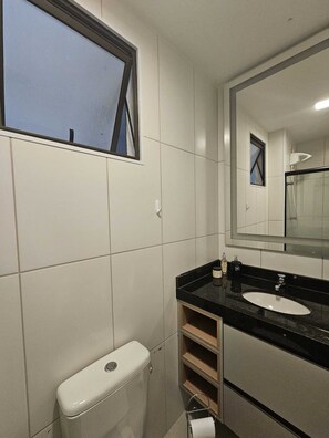 Et badeværelse med toilet, håndvask, spejl og et vindue.