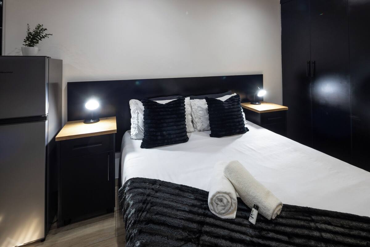 A hotel room with a bed, two bedside tables, a nightstand, a wall-mounted TV, and a refrigerator.