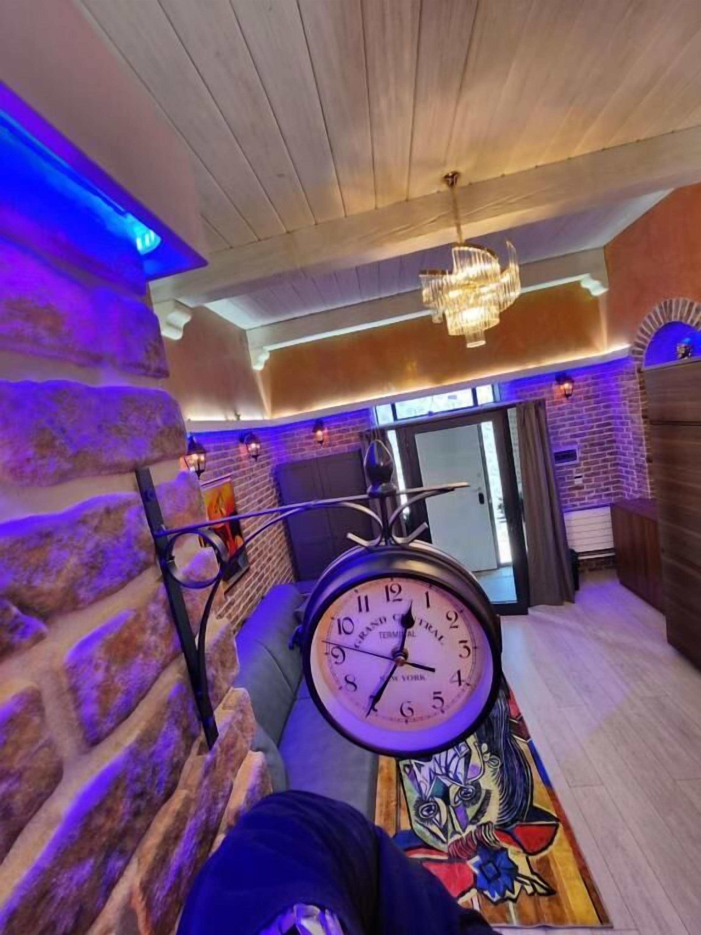 Ein Zimmer mit Steinwand, einer Uhr, einem Chandelier und einer Tür zu einem weiteren Raum.