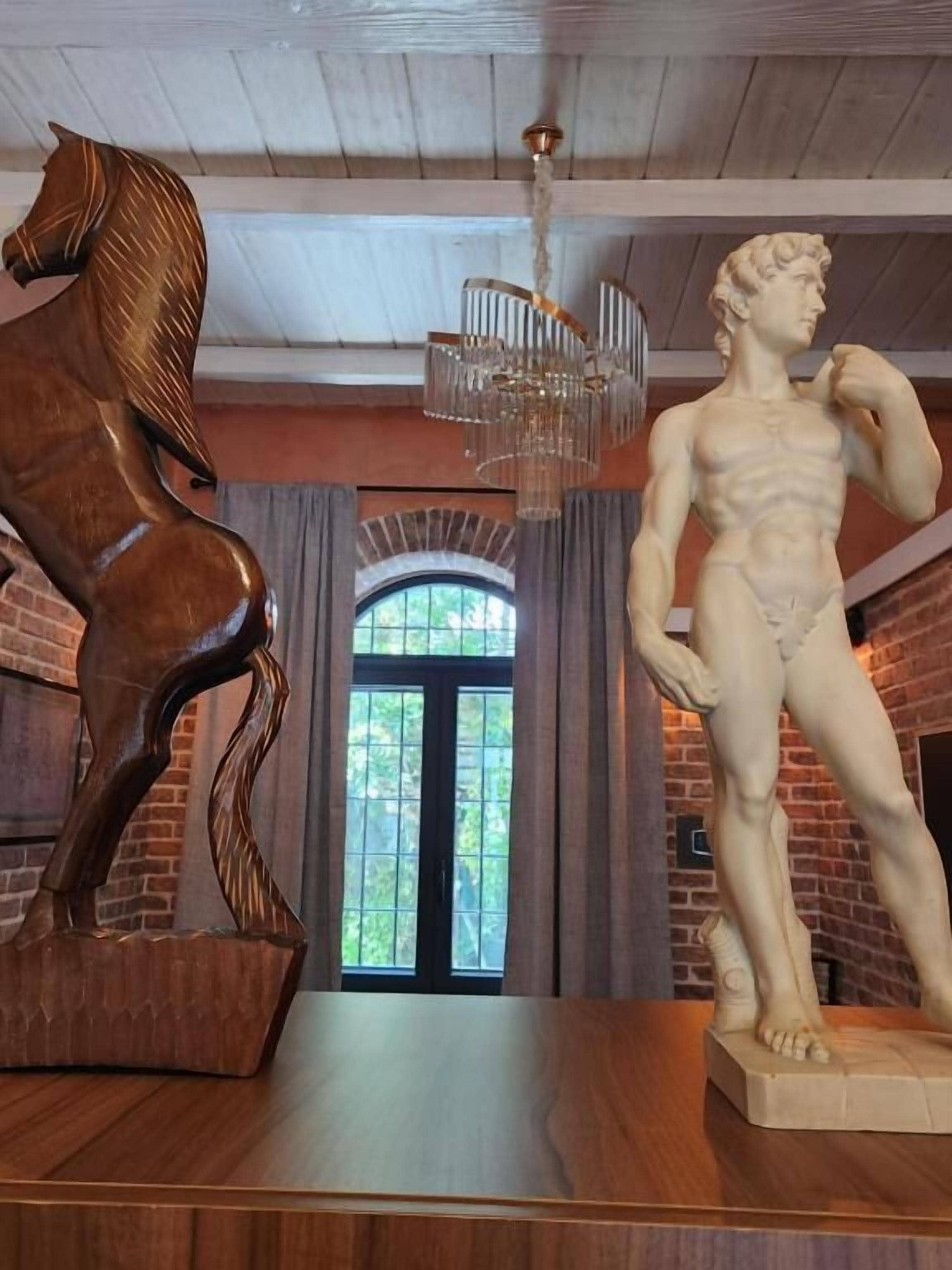 Et værelse med en stor træhest skulptur, en klassisk statue og en lysekrone.