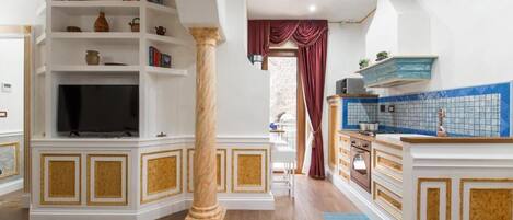 A spacious living area with a television, a large column, and a kitchen with blue tiles.