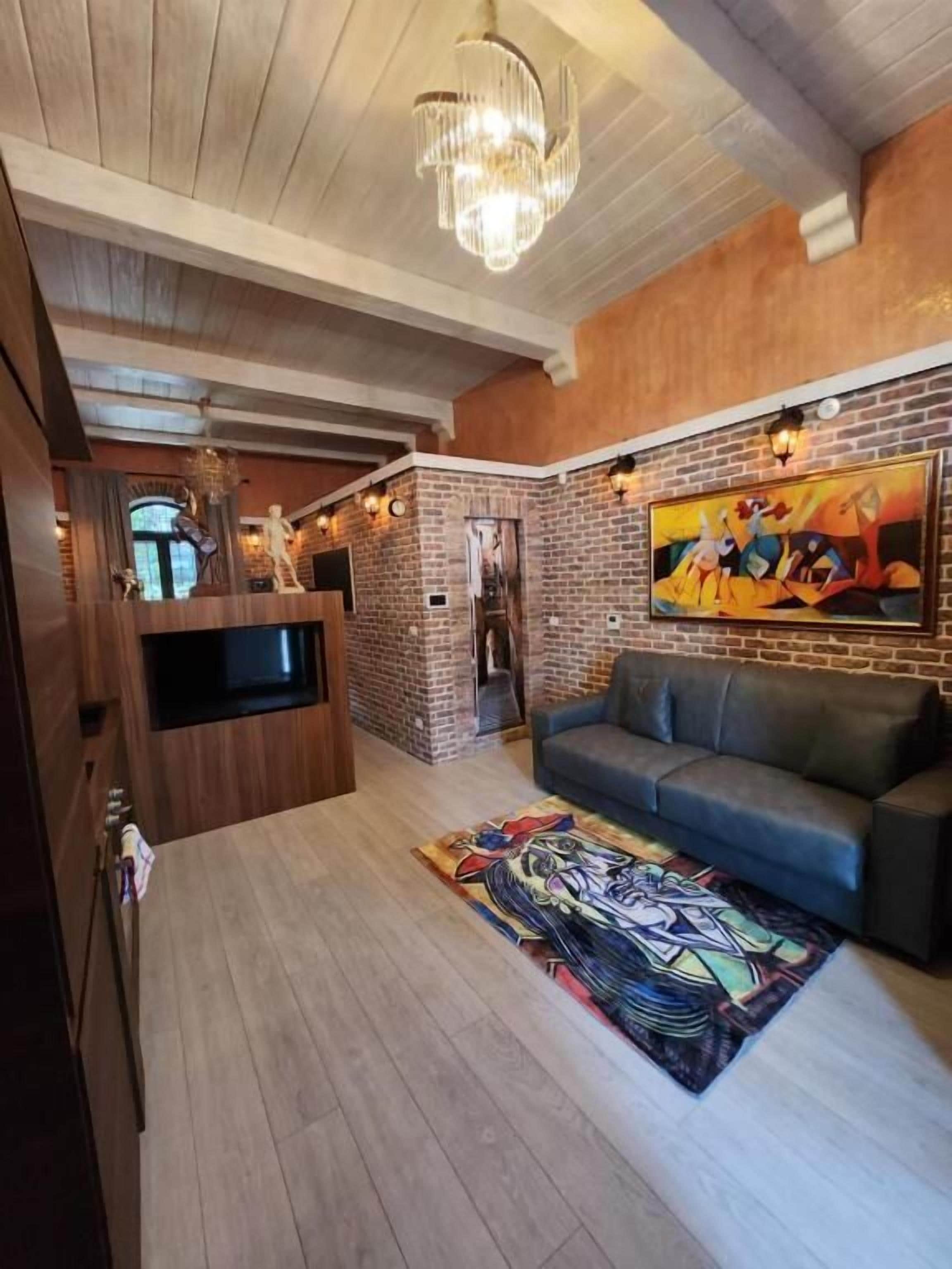 Ein modernes Wohnzimmer mit Backsteinwand, einem blauen Sofa, einer Kronleuchter und einem farbenfrohen Teppich.