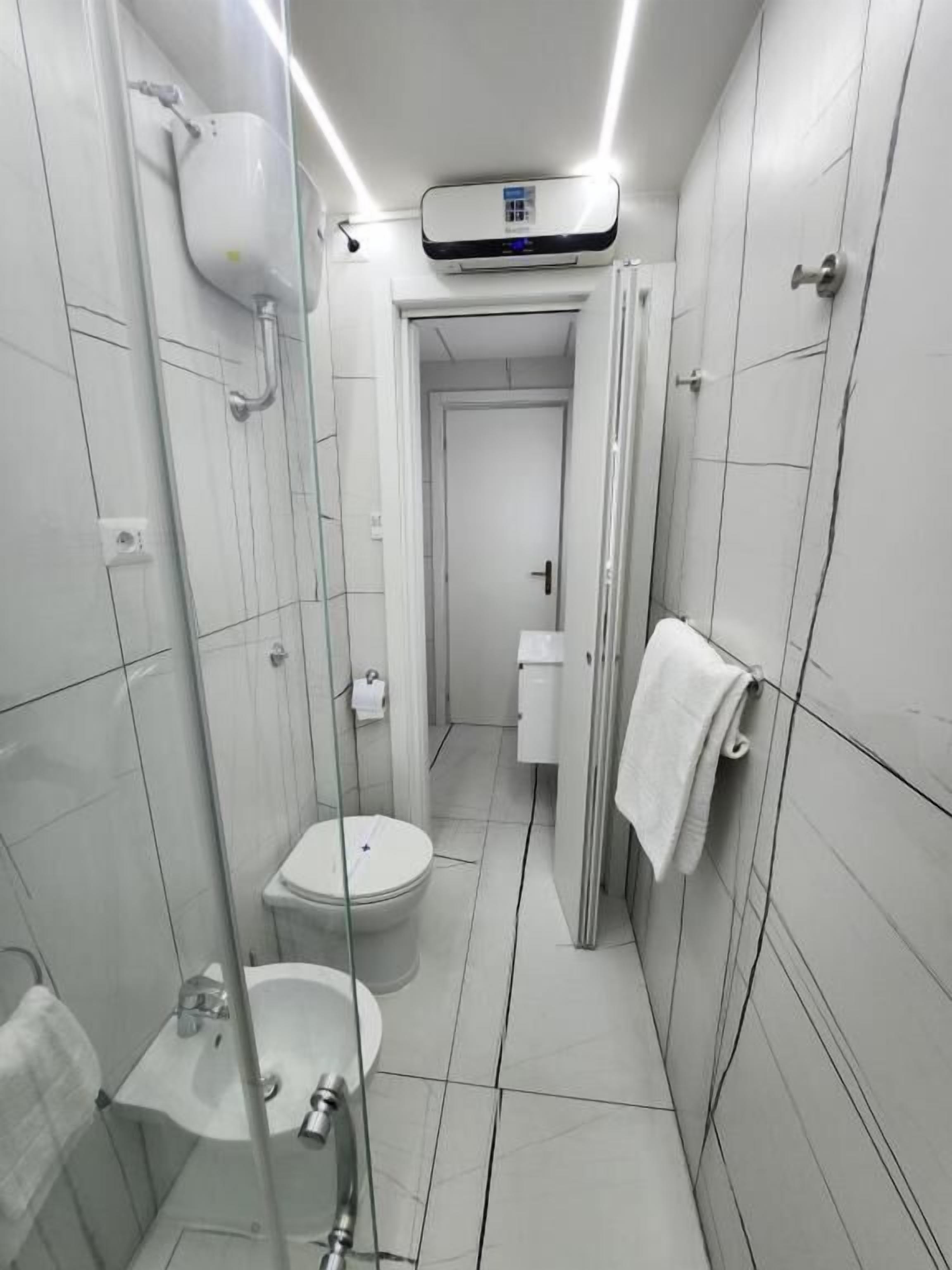 Ein schmales Badezimmer mit Toilette, Bidet und Waschbecken, alles in Weiß.