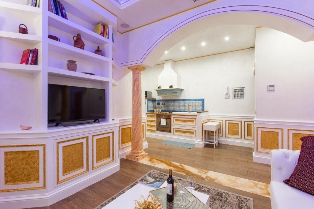 Una sala de estar con televisor, estanterías, un comedor con mesa y sillas, y una cocina al fondo.